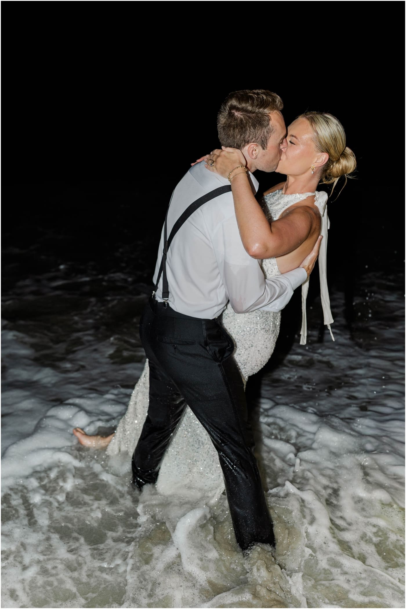 bride and groom kissing in ocean after their wedding reception at the coral bay club