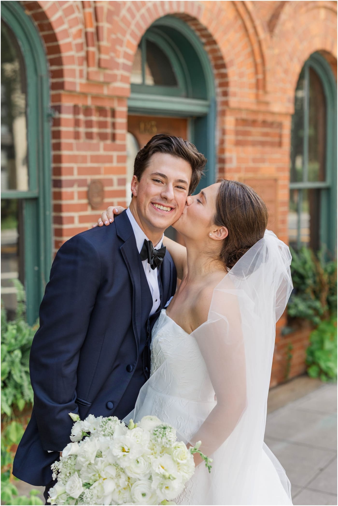 Bride kissing groom on cheek outside of Huguenot loft in downtown Greenville 