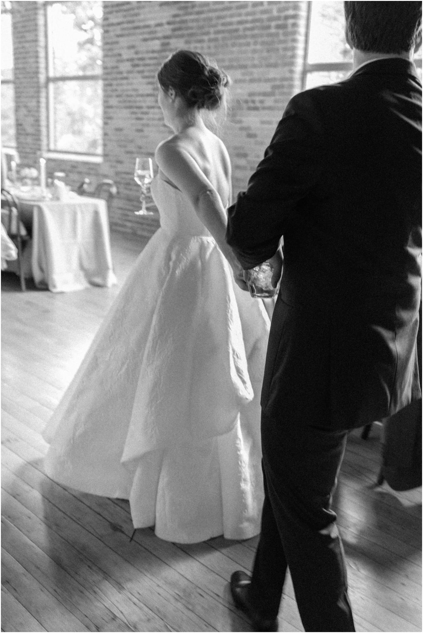 black and white blurry image of bride holding grooms hand and leading him to reception