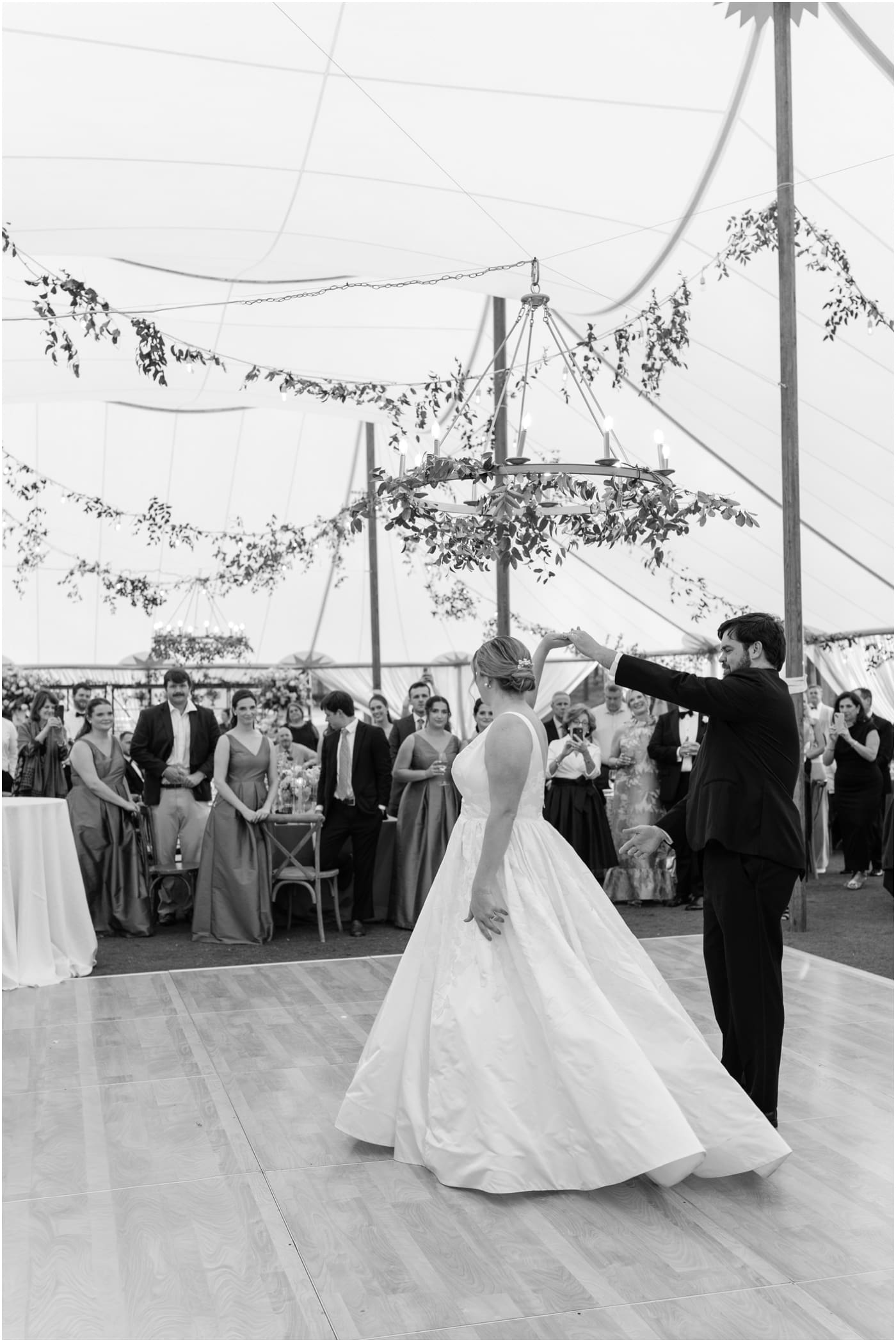 black and white of groom spinning bride during first dance at their tented reserve at lake keowee wedding