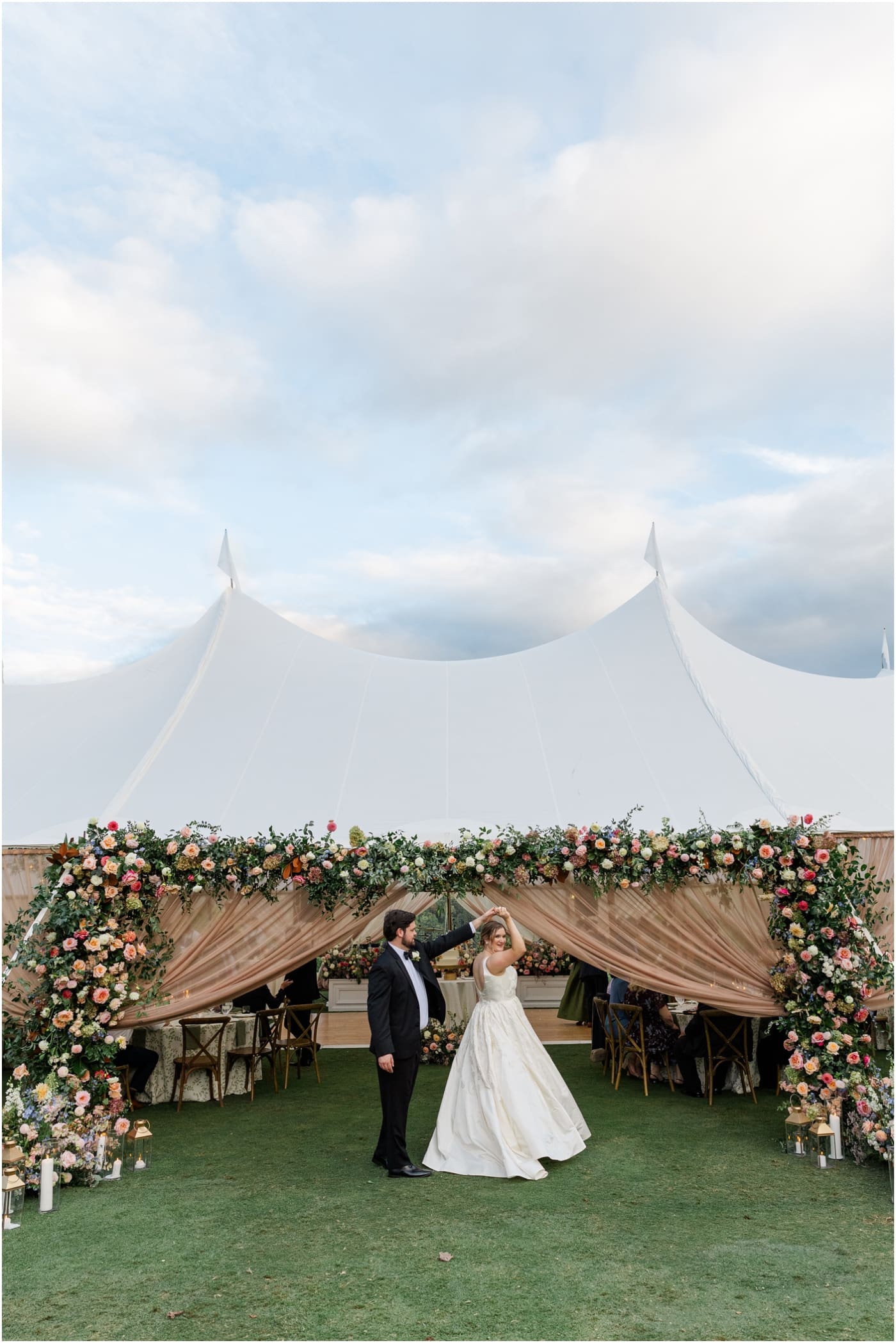 Groom spinning bride in front of floral arch on sailcloth tent at their reserve at lake keowee wedding